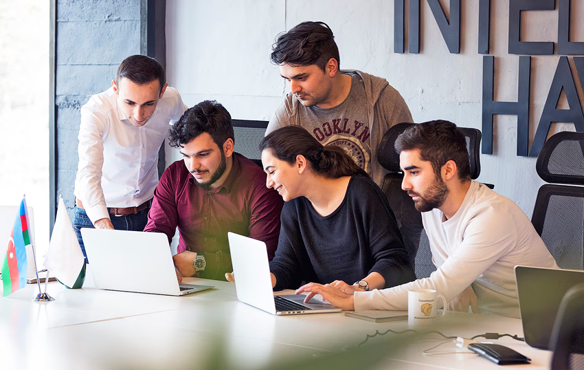 in this image, 5 employees are sitting on the chair with laptops and discussing with others.