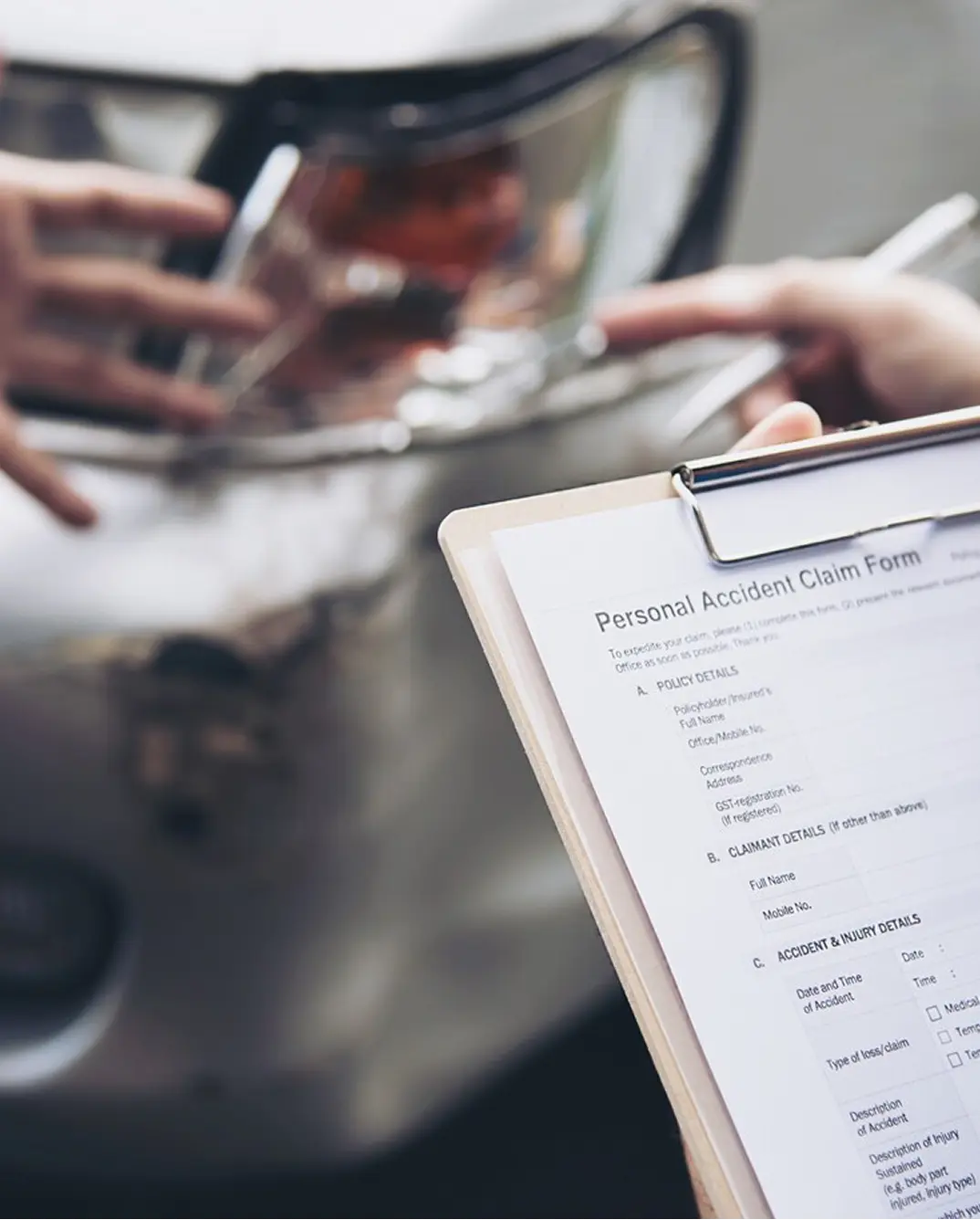 A person fills out an accident claim form beside a damaged car.